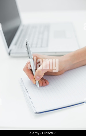 Close up of a hand writing notes by laptop Stock Photo
