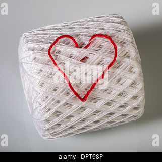 Knitted red heart on white ball of yarn. Stock Photo