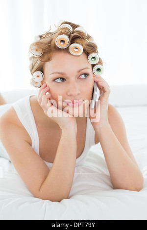 Woman in hair curlers using cellphone while lying in bed Stock Photo