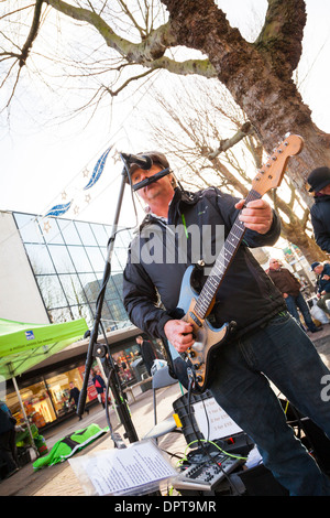 Busker playing electric guitar and mouth organ in town centre. Stock Photo