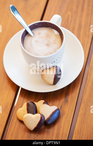 Cup of coffee served with chocolate-dipped heart shaped biscuits Stock Photo