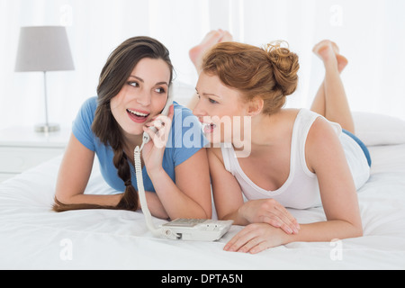 Happy woman with friend using phone in bed Stock Photo