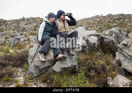 Couple sitting on rock with binoculars while on a hike Stock Photo