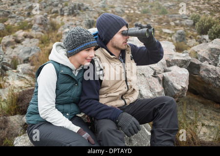 Couple sitting on rock with binoculars while on a hike Stock Photo