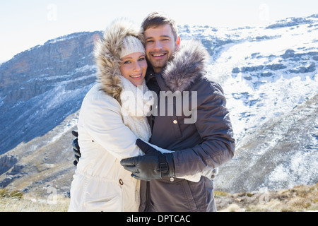Loving couple in fur hood jackets against snowed mountain range Stock Photo