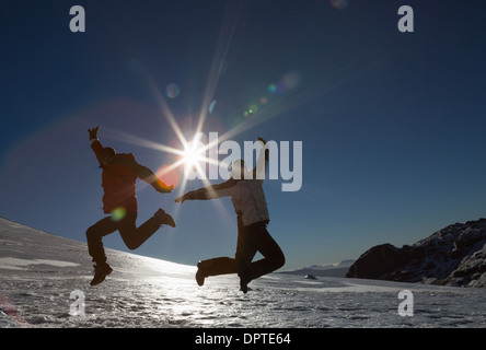Silhouette couple jumping on snow against sun and blue sky Stock Photo