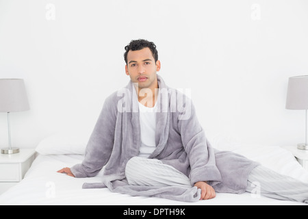 Relaxed young man in bathrobe sitting on bed Stock Photo