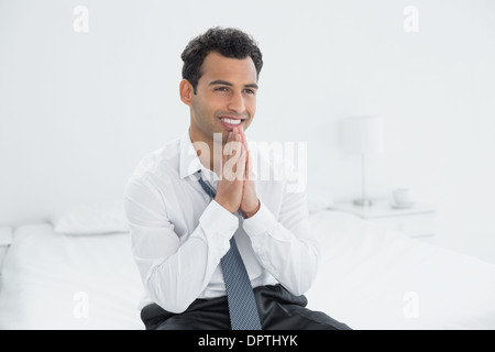Happy thoughtful businessman sitting on bed Stock Photo