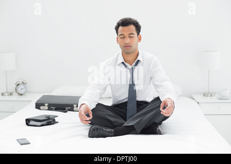 Relaxed young businessman sitting in lotus pose on bed Stock Photo