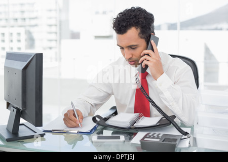 Businessman writing notes while on call at office Stock Photo