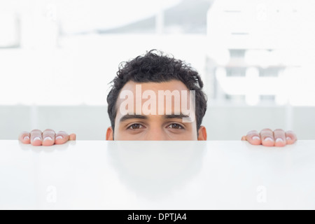 Businessman peeking behind the desk at office Stock Photo