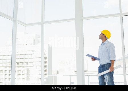 Handyman in hard hat with clipboard and blueprint looking at window Stock Photo