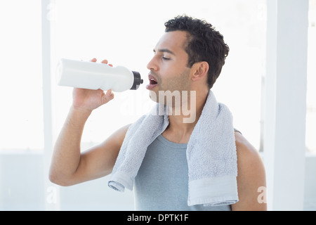 Man with towel around neck drinking water in fitness studio Stock Photo