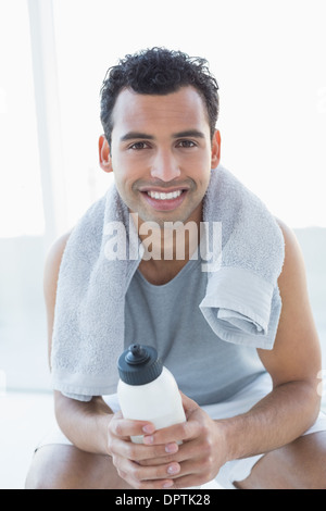 Man with towel around neck holding water bottle in fitness studio Stock Photo