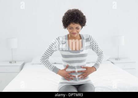 Casual woman with stomach pain sitting in bed Stock Photo