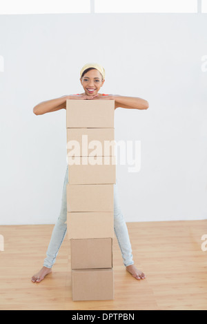 Smiling woman moving in new house with a stack of boxes Stock Photo