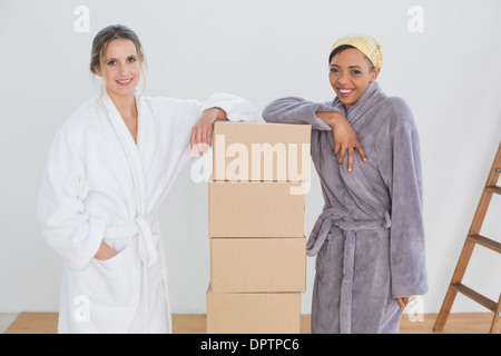 Female friends in bathrobes by boxes in new house Stock Photo