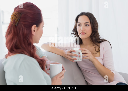 Young female friends chatting over coffee at home Stock Photo