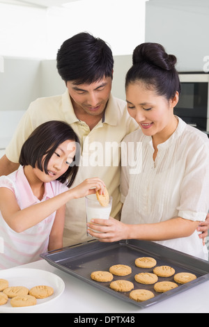 Girl enjoying cookies and milk with parents in kitchen Stock Photo