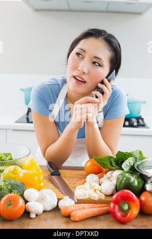 Woman using mobile phone in front of vegetables in kitchen Stock Photo