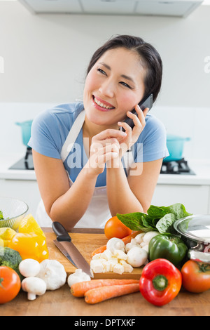 Woman using mobile phone in front of vegetables in kitchen Stock Photo