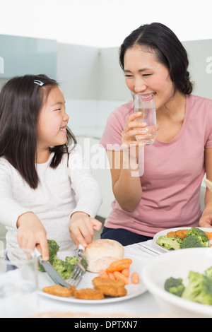 Mother watching little girl eat food in kitchen Stock Photo