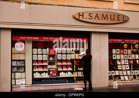 H Samuel Jewellers retail assistant putting up January Sales posters on the windows advertising Diamond Pendants in Dundee, UK Stock Photo