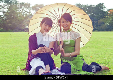 To young women holding umbrellas in traditional Vietnamese dress smiling at camera kneeling Stock Photo