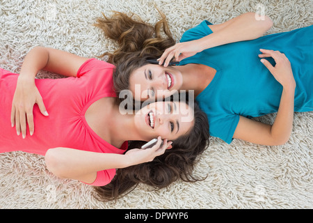 Two female friends lying on rug and using cellphone Stock Photo
