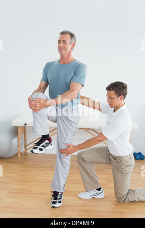 Therapist helping man with stretching exercises in gym hospital Stock Photo