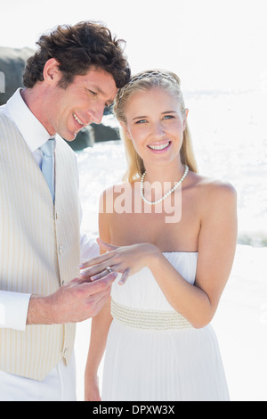 Handsome man placing ring on happy brides finger Stock Photo