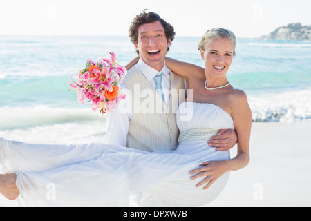 Groom carrying his pretty blonde wife smiling at camera Stock Photo