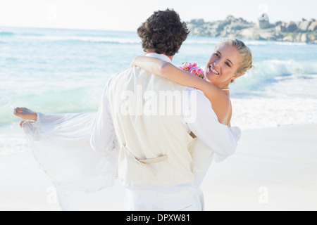 Handsome groom carrying his beautiful wife smiling at camera Stock Photo