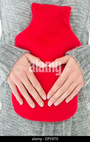 Mid section of a woman holding red hot water bag on abdomen Stock Photo