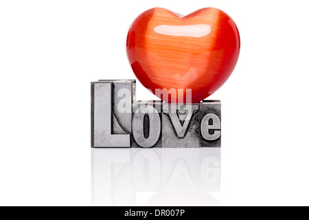 Love in old mixed font metal letterpress blocks with a red gemstone heart on top, isolated on a white background. Stock Photo