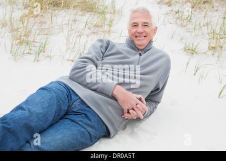Smiling senior man relaxing on sand at beach Stock Photo