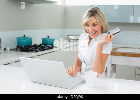 Cheerful woman doing online shopping in the kitchen Stock Photo