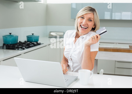 Cheerful woman doing online shopping in kitchen Stock Photo