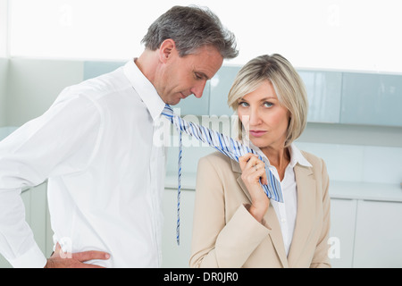 Woman holding a man by his neck tie in kitchen Stock Photo