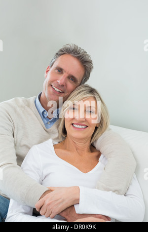 Happy couple embracing while sitting on sofa at home Stock Photo