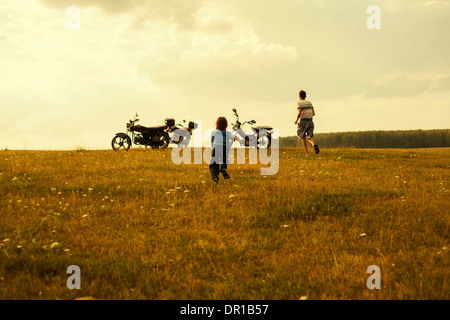 Boys running to motorcycles in rural landscape Stock Photo