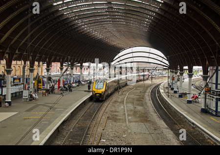 Interior view of trainshed with iron & glass roof, stationary trains & people waiting on platfom - York Railway Station, North Yorkshire, England, UK. Stock Photo