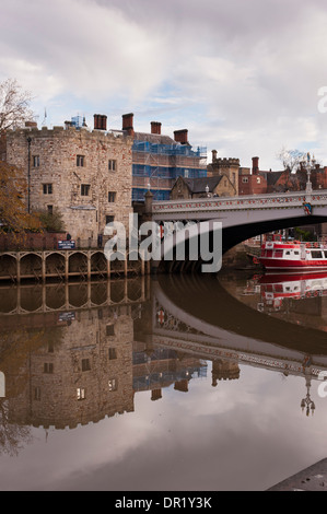 Lendal Bridge, stone tower on River Ouse bank, moored city cruise boat reflected in water, people walking - scenic York, North Yorkshire, England, UK. Stock Photo
