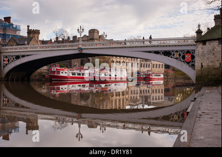 People crossing Lendal Bridge & moored cruise boats reflected in calm water of River Ouse - picturesque York city centre, North Yorkshire, England UK. Stock Photo