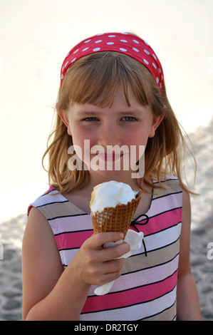 portait of little blonde girl eating a vanilla ice-cream on holiday in a striped white and pink dress and polka dot hair-band Stock Photo