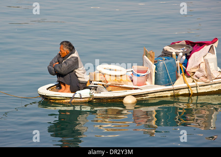 Sad Looking Old Chinese man sits on the bow of an overloaded boat in the Causeway Bay Typhoon Shelter, Hong Kong. Stock Photo
