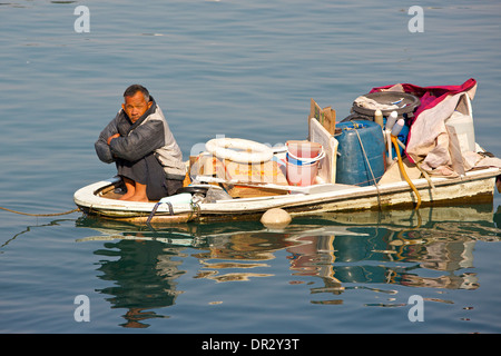 Old Chinese man sits on the bow of an overloaded boat in the Causeway Bay Typhoon Shelter, Hong Kong. Stock Photo