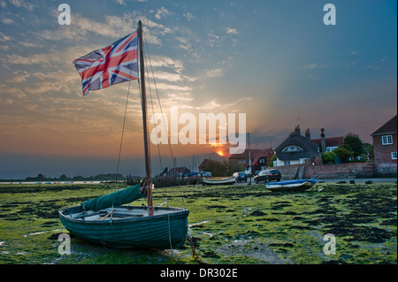 A dinghy flies a Union Jack flag from it's mast with a setting sun behind it Stock Photo