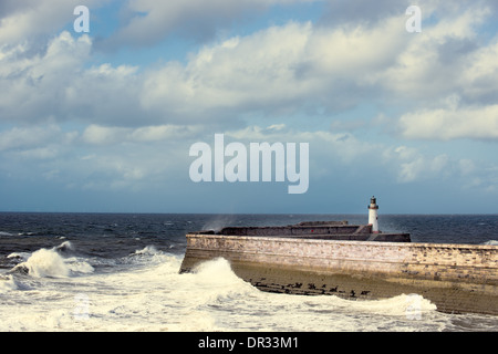 Waves crashing against the sea wall with lighthouse at Whitehaven, England, UK Stock Photo