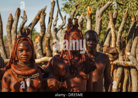 Himba family of four poses outdoors in front of animal coral in Damaraland, Namibia, Africa Stock Photo